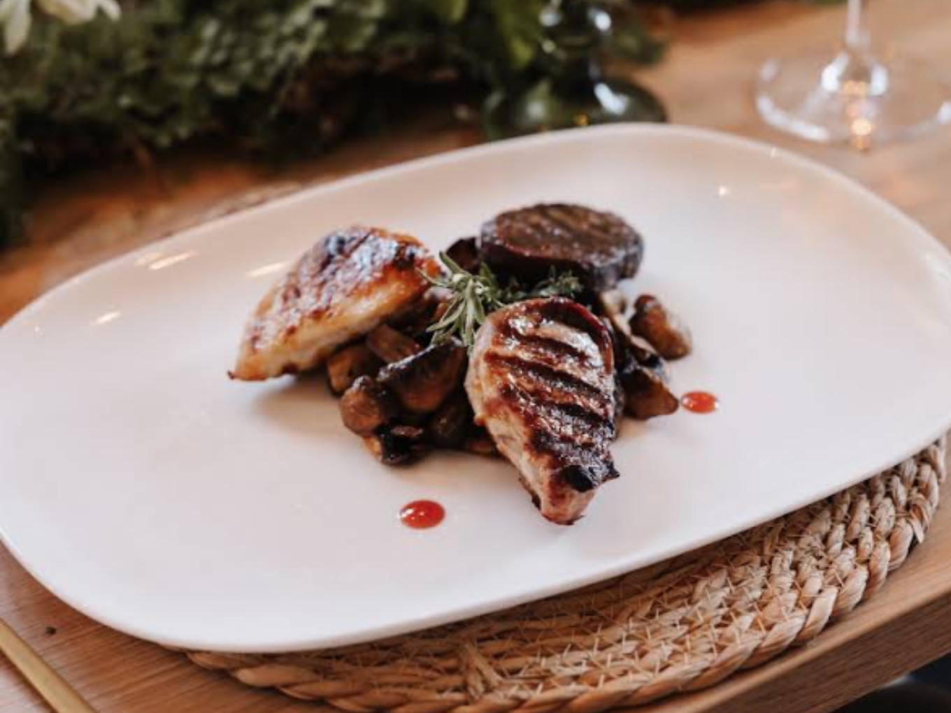 Gegrillte Fleischmedaillons auf Pilzen, mit Rosmarin und Saucenpunkten auf einem weißen Teller angerichtet.