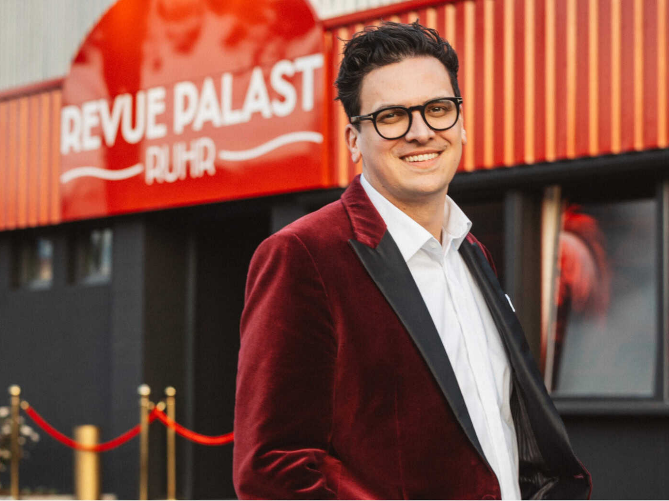 Mann im Anzug vor dem Revue Palast Ruhr mit Leuchtschrift und rotem Samtvorhang