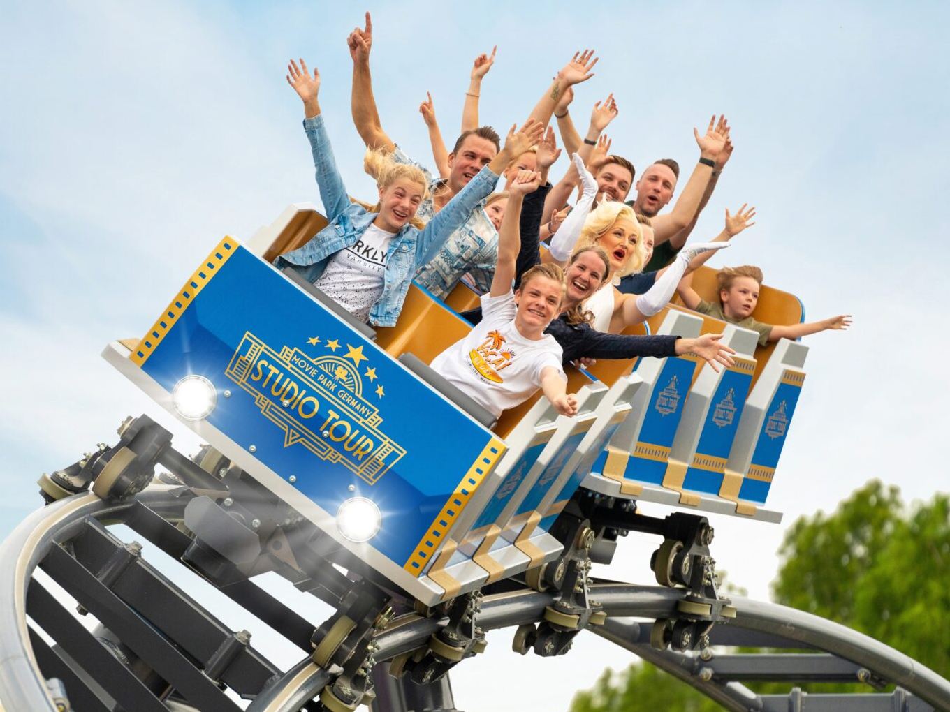 Menschen fahren lachend in einer blauen Achterbahn mit der Aufschrift „Studio Tour“.
