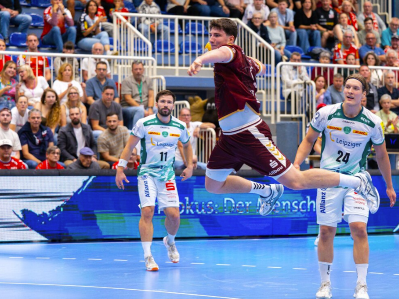 Ein Handballspieler von TUSEM Essen springt in der Halle zum Wurf, während zwei Leipziger Gegner zuschauen