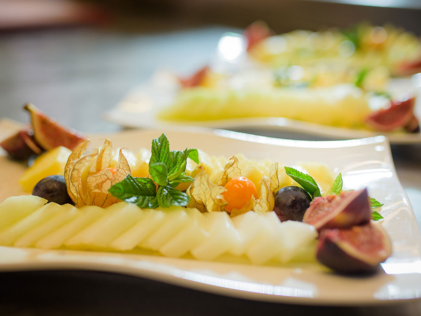 Frisch angerichtete Melonenscheiben mit Trauben, Feigen, Physalis und Minze auf einem weißen Teller.