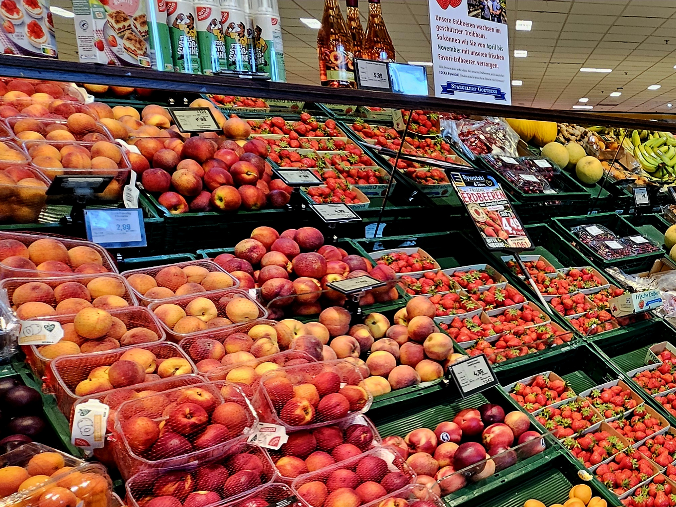 Frische Erdbeeren und Pfirsiche in Plastikschalen im Supermarktregal unter Beleuchtung