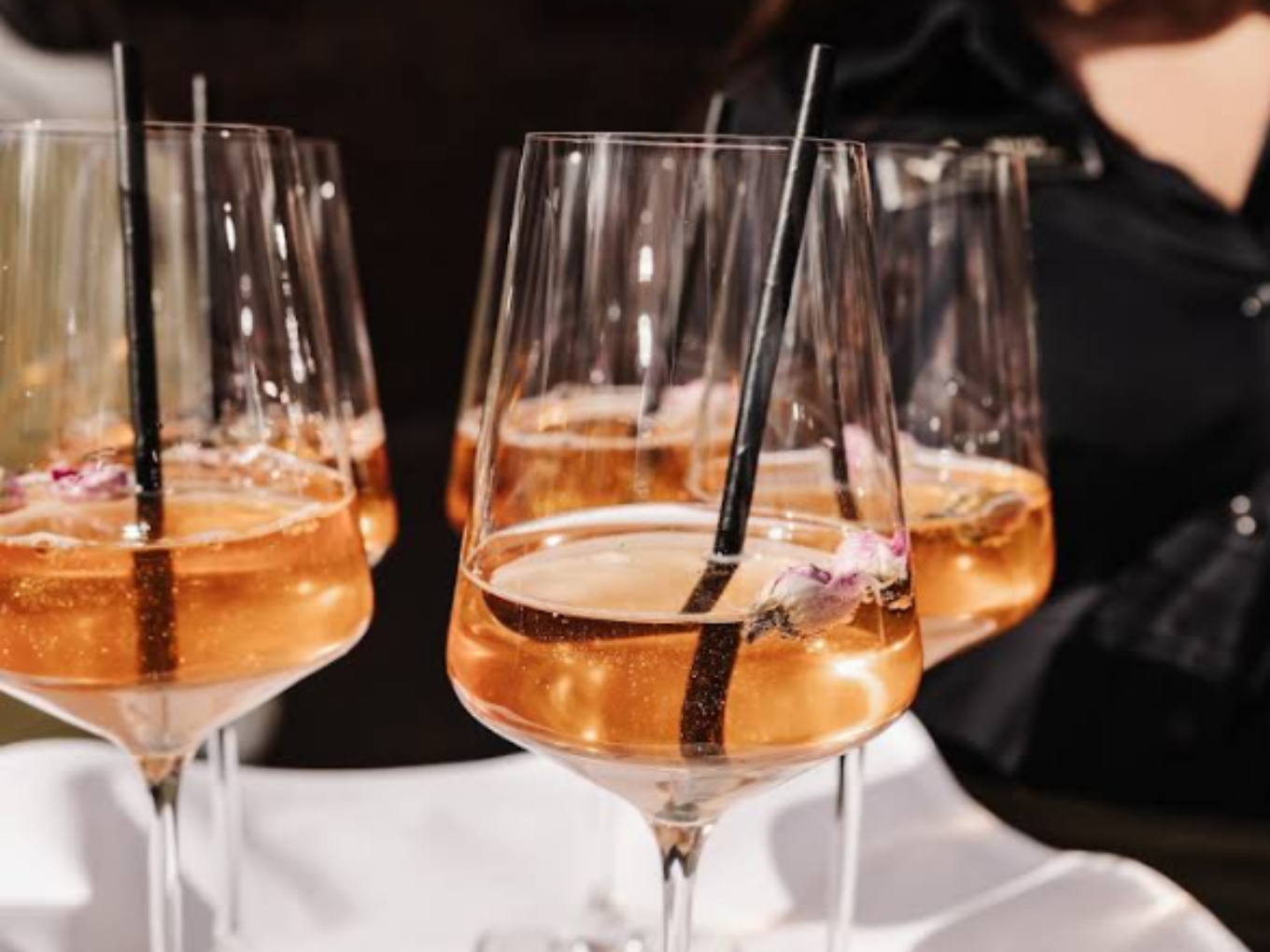 Mehrere Gläser mit roséfarbenem Aperitif, schwarzen Trinkhalmen und essbaren Blüten im Restaurant Am Jäger.