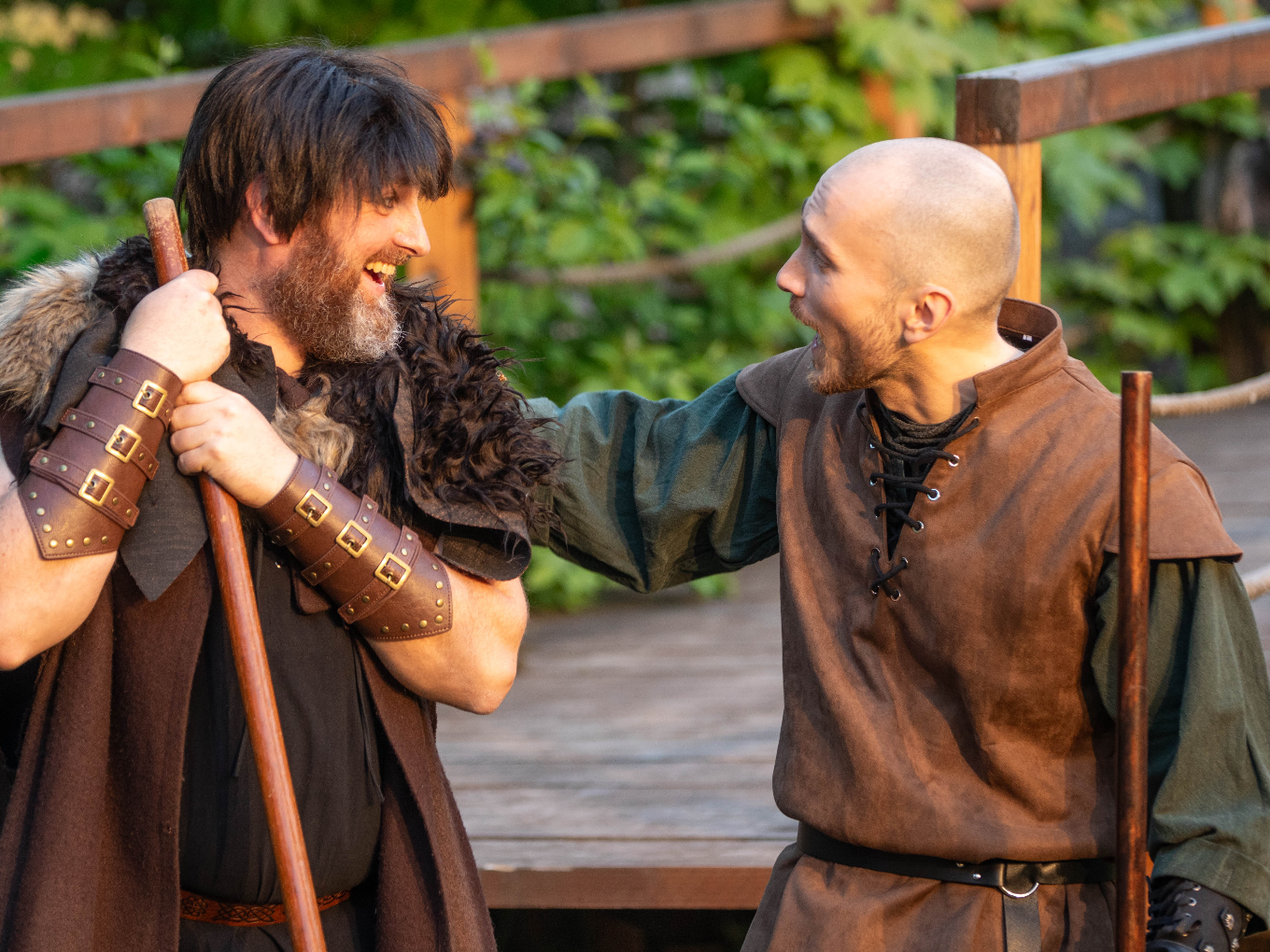 Robin Hood begrüßt lachend einen Gefährten mit Kampfstab.