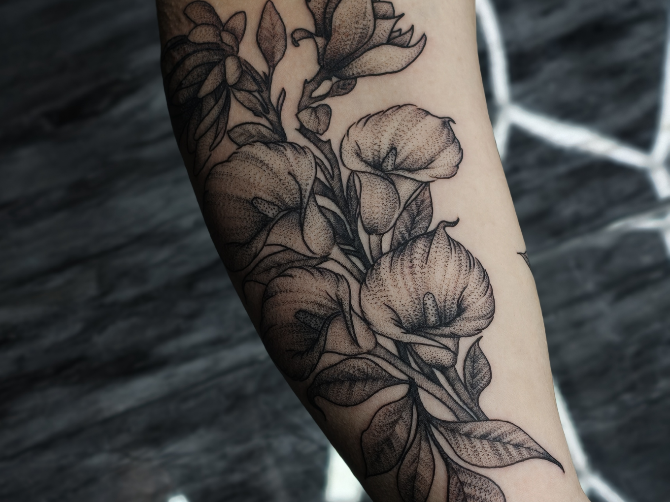 Florales Blackwork-Tattoo mit Calla-Blüten und Blättern am Arm
