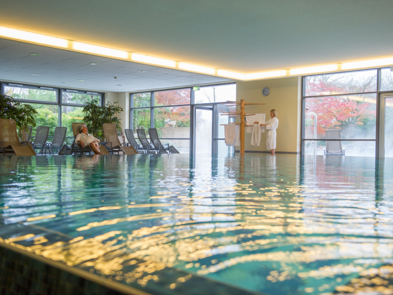 Helles Innenbecken der Grugapark-Therme mit Ruheliegen und Blick ins Grüne.