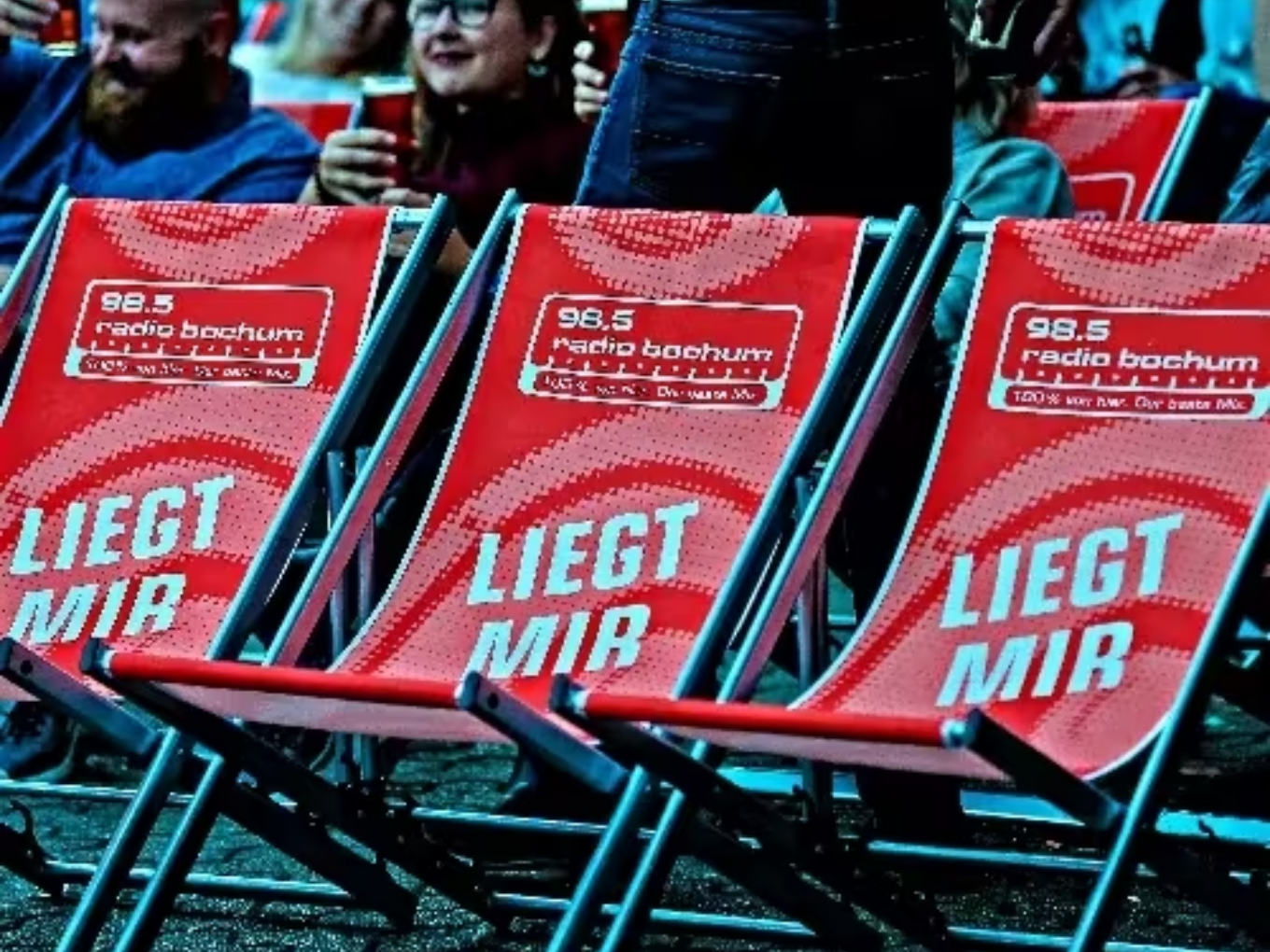 Rote Liegestühle mit „98.5 Radio Bochum“ und dem Schriftzug „Liegt mir“ beim Open-Air-Kino, Menschen im Hintergrund.