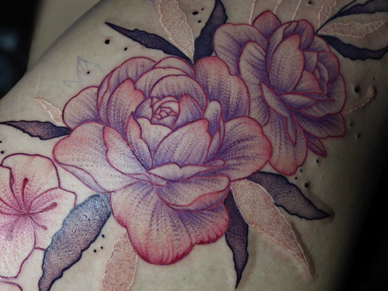 Florales Tattoo mit rosa-violetten Blüten und dunklen Blättern auf dem Oberschenkel.
