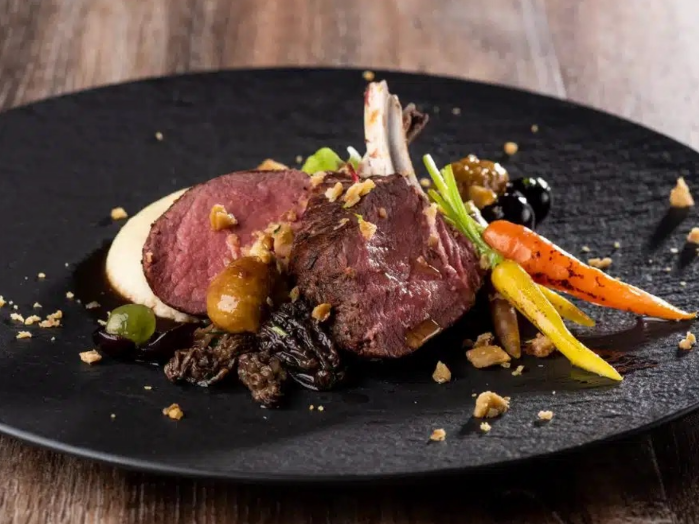 Fein angerichtetes rosa gebratenes Fleisch mit Morcheln, bunten Möhren, Püree und dunkler Sauce.